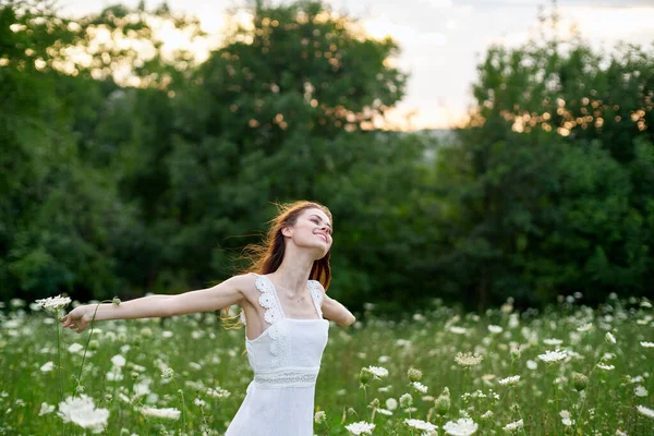 Glad kvinna på ett fält med blommor i en vit klänning i naturen — Stockfoto