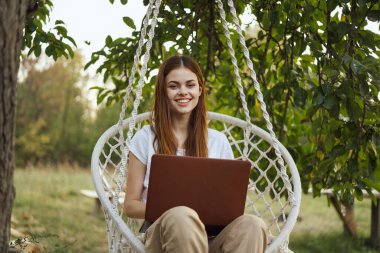 Bilgisayarlı kadın dışarıda hamakta dinleniyor.