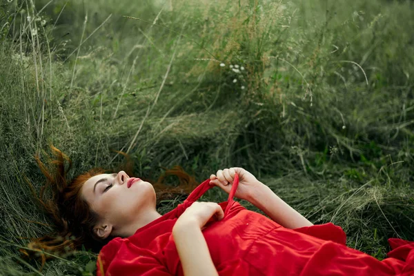 Mujer bonita en vestido rojo se encuentra en la hierba en el campo naturaleza aire fresco —  Fotos de Stock
