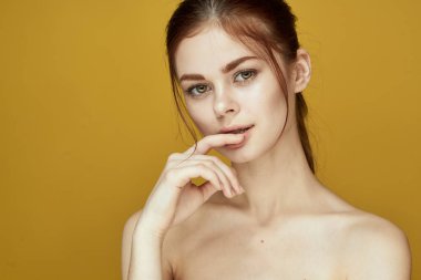 Çıplak omuzlu, beyaz tenli, sarı arkaplan pozu veren bir kadın.