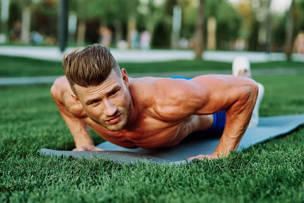 athletic man with pumped up muscular body in the park doing exercise