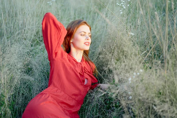 Pretty woman in red dress lies on the grass nature sun — Stock Photo, Image