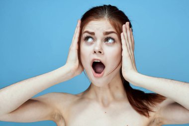 Çıplak omuzlu, at kuyruklu, mavi arka plan pozu veren bir kadın.