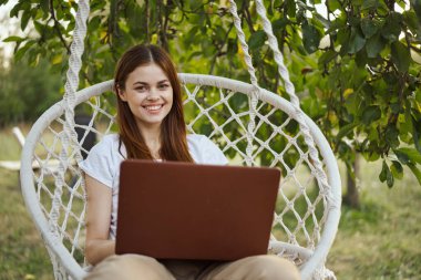 Hamakta dizüstü bilgisayar teknolojisiyle gülümseyen kadın.