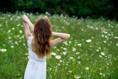 Çiçek tarlasında beyaz elbiseli bir kadın özgürce yürüyor.