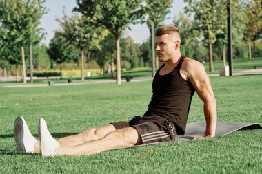 Sportif adam parkta çimlerde oturuyor.