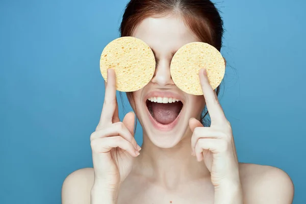 Woman with sponges in hands bare shoulders clear skin blue background — Stock Photo, Image