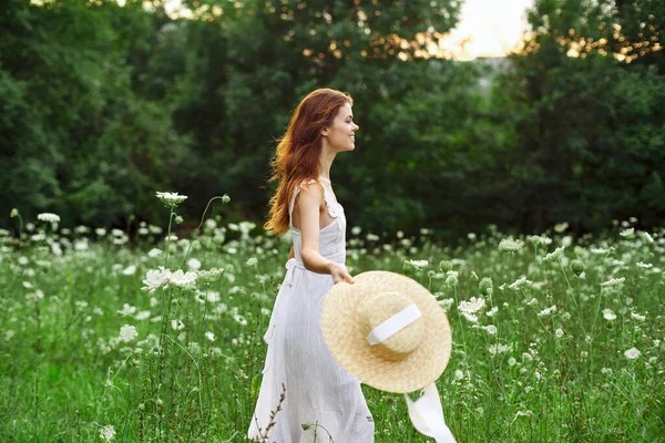 Kvinna i vit klänning hatt håller blommor natur promenad — Stockfoto