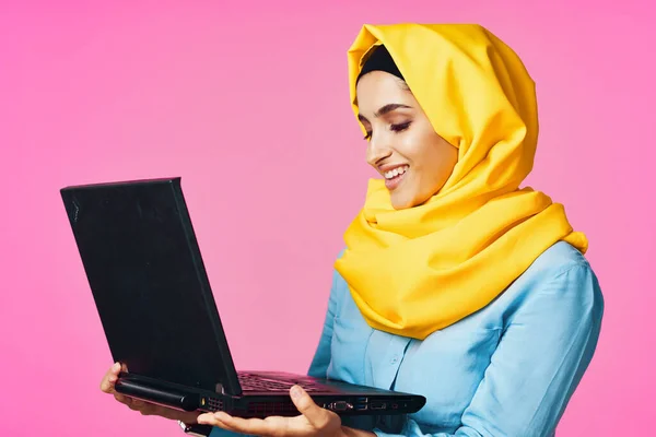 带黄色头巾的穆斯林妇女，带有笔记本电脑技术学生粉色背景 — 图库照片
