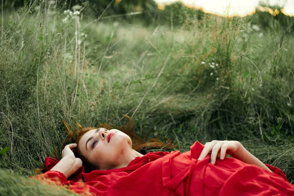 Pretty woman in red dress lies on the grass freedom landscape — Stock Photo, Image