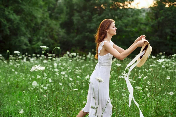 Donna in abito bianco cappello che tiene fiori natura passeggiata — Foto Stock