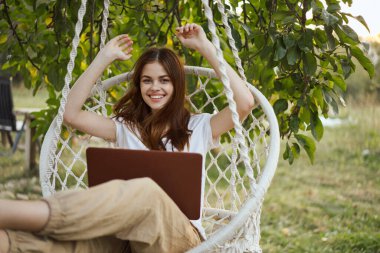 Hamakta dizüstü bilgisayarı dinlenen neşeli bir kadın.