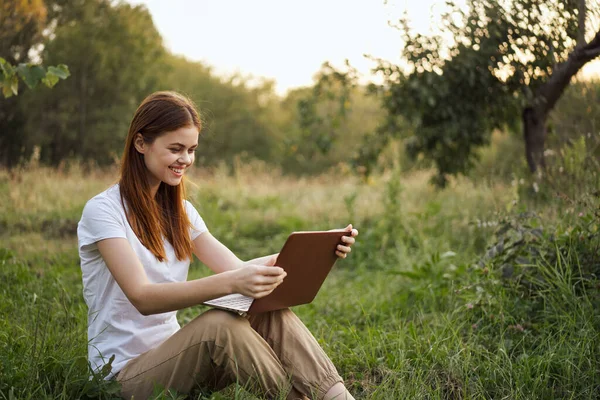 Kvinna utomhus sitter på gräset med bärbar sommarsemester kommunikation — Stockfoto