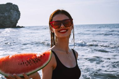 Ellerinde karpuz olan siyah mayo giymiş güzel bir kadın.