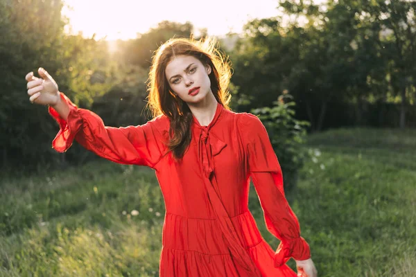 Attraktiv kvinna i röd klänning poserar i naturen grönt gräs — Stockfoto