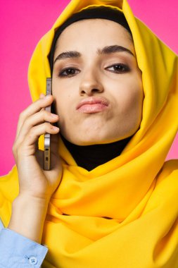 Sarı tesettürlü müslüman kadın telefon teknolojisi pembe arka planda konuşuyor.