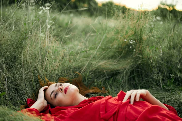 Žena v červených šatech ležící na trávě čerstvý vzduch příroda romantika — Stock fotografie