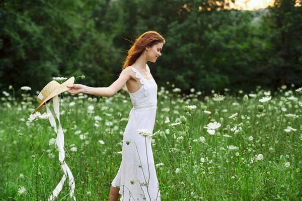 Femme en robe blanche chapeau tenant fleurs nature promenade — Photo