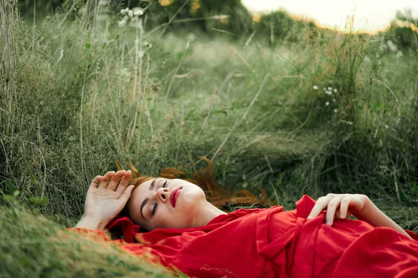 Žena v červených šatech ležící na trávě čerstvý vzduch příroda romantika — Stock fotografie