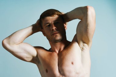 Kaslı vücutlu vücut geliştirici mavi arka plana basar