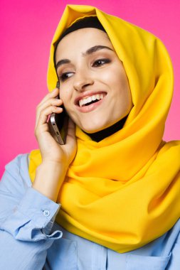 Sarı tesettürlü müslüman kadın telefon teknolojisi pembe arka planda konuşuyor.