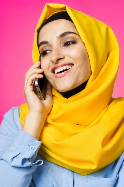 Mujer musulmana en hijab amarillo hablando sobre la tecnología del teléfono de fondo rosa —  Fotos de Stock