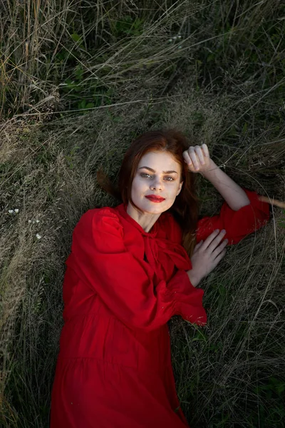 Όμορφη γυναίκα με κόκκινο φόρεμα βρίσκεται στο γρασίδι ποζάροντας πάνω άποψη — Φωτογραφία Αρχείου