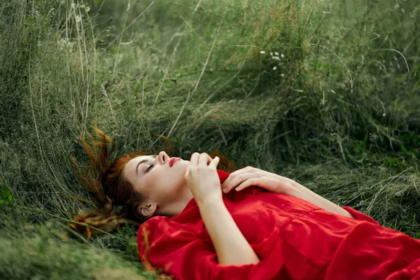 Pretty woman in red dress lies on the grass in the field nature fresh air — Stock Photo, Image