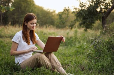 Dışarıda çimlerde oturan bir kadın dizüstü bilgisayarlı yaz tatili iletişimiyle