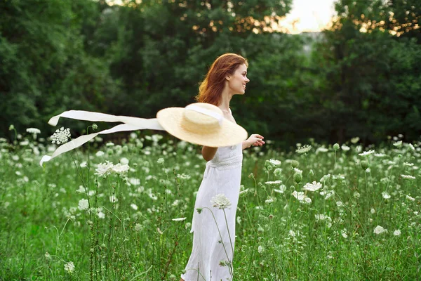Kvinna i vit klänning hatt håller blommor natur promenad — Stockfoto