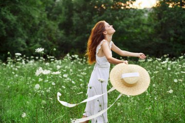 Beyaz şapkalı kadın elinde çiçekler, doğa yürüyüşü.
