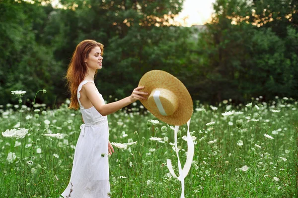 Donna in abito bianco e cappello in un campo con stile di vita fiori — Foto Stock
