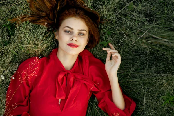 Vacker kvinna i röd klänning ligger på gräset landskap frihet — Stockfoto