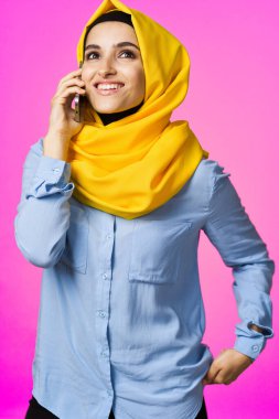 Sarı tesettürlü müslüman kadın telefonda pembe teknolojiyle konuşuyor.