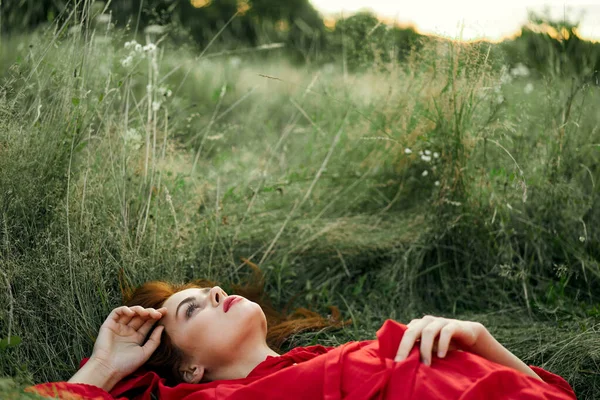 Hübsche Frau im roten Kleid liegt auf dem Gras — Stockfoto