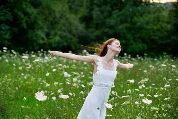 Veselá žena na poli s květinami v bílých šatech v přírodě — Stock fotografie