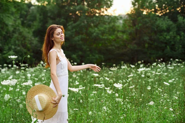 Çiçekli bir tarlada beyaz elbiseli ve şapkalı bir kadın. — Stok fotoğraf