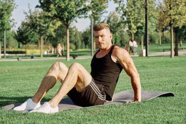 Sportif adam parkta çimlerde oturuyor.