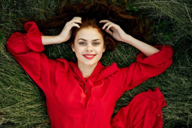 Kırmızı elbiseli kadın çimenlerin üzerinde uzanmış özgürlüğe bakıyor.