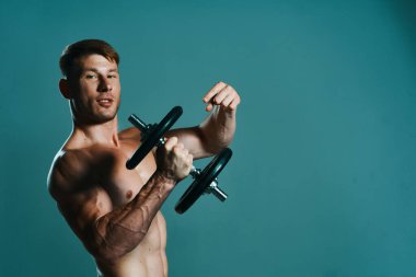 Elinde dambıllar olan atletik bir adam kas egzersizi yapıyor.