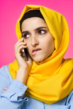 Sarı tesettürlü müslüman kadın telefon teknolojisi pembe arka planda konuşuyor.