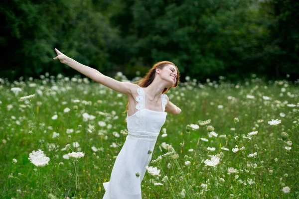 Mulher alegre em um campo com flores em um vestido branco na natureza — Fotografia de Stock