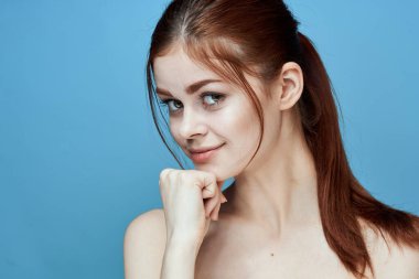 Çıplak omuzlu, at kuyruklu, mavi arka plan pozu veren bir kadın.