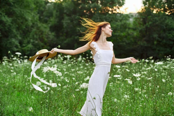 Donna in abito bianco cappello che tiene fiori natura passeggiata — Foto Stock