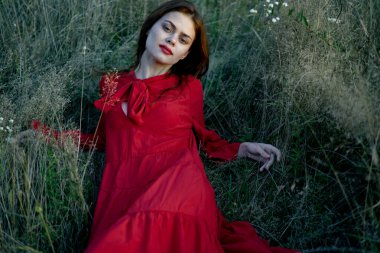 Kadın kırmızı bir elbiseyle çimlerin üzerinde yatıyor.
