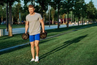 Dambılı erkek sporcu parkı CrossFit egzersizi yapıyor.