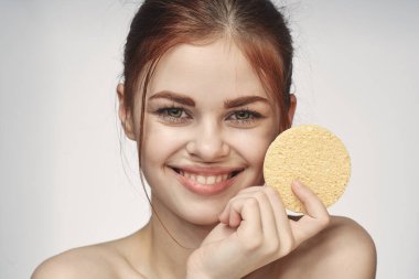 Ellerinde süngerle çıplak omuzlarıyla cilt bakımı yapan bir kadın.