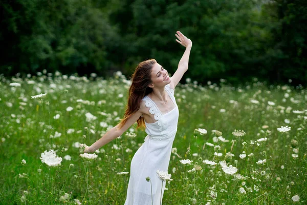 Glad kvinna på ett fält med blommor i en vit klänning i naturen — Stockfoto