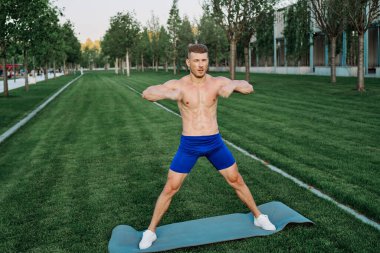 Mavi şortlu atletik adam parkta çalışıyor.