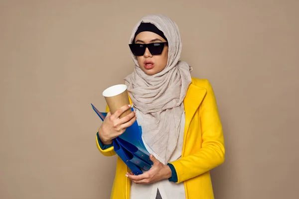 Mulher em óculos de sol no hijab uma xícara de café bege fundo — Fotografia de Stock